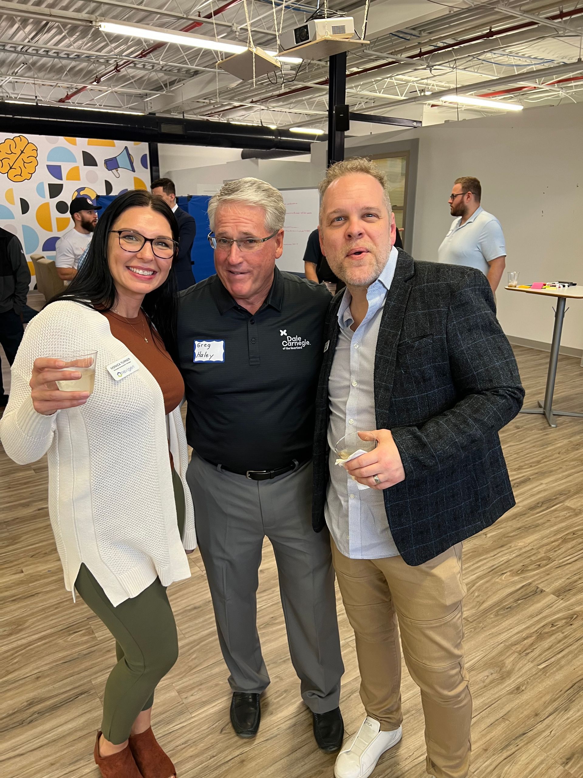 Three people smiling at an indoor event. A woman in a white sweater and two men pose for a photo.
