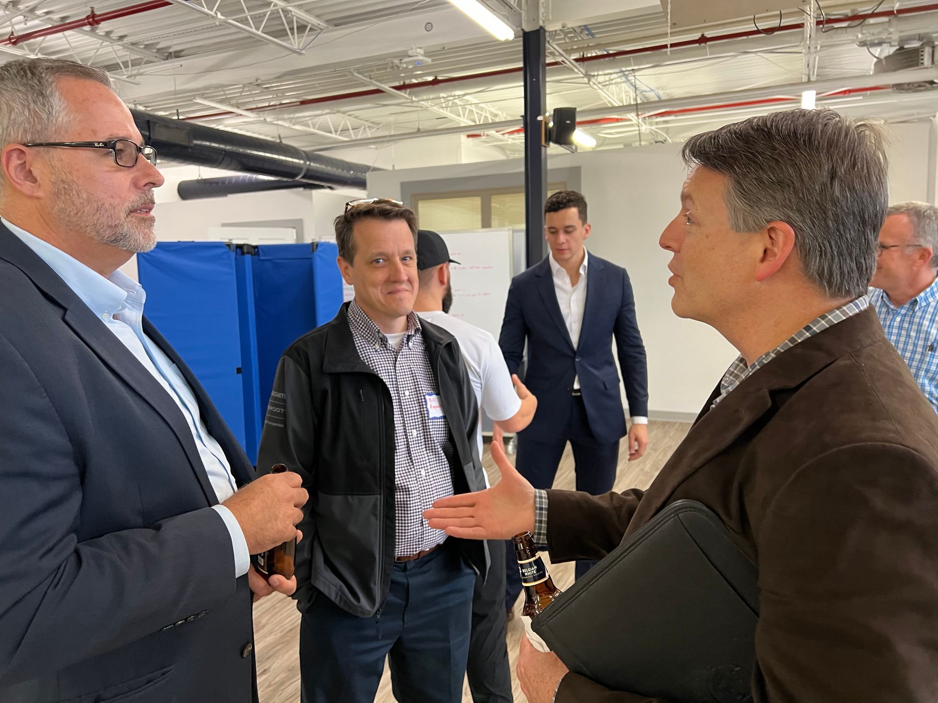 Men in business attire conversing in a modern office space. One man gestures with his hand.
