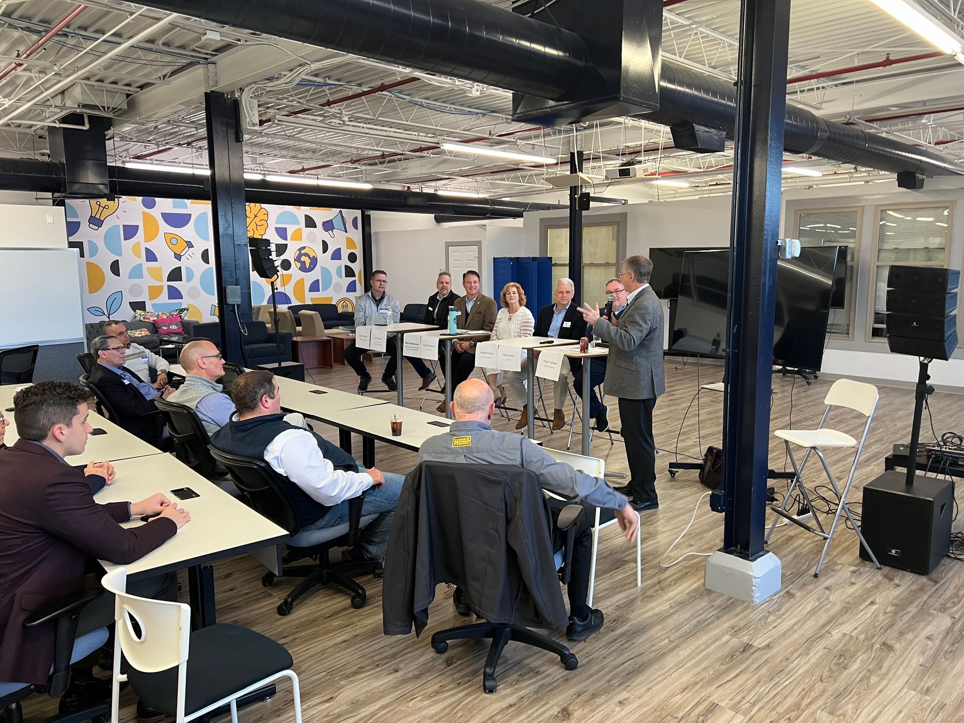 Panel of people seated at a table, with an audience, in a modern office space.