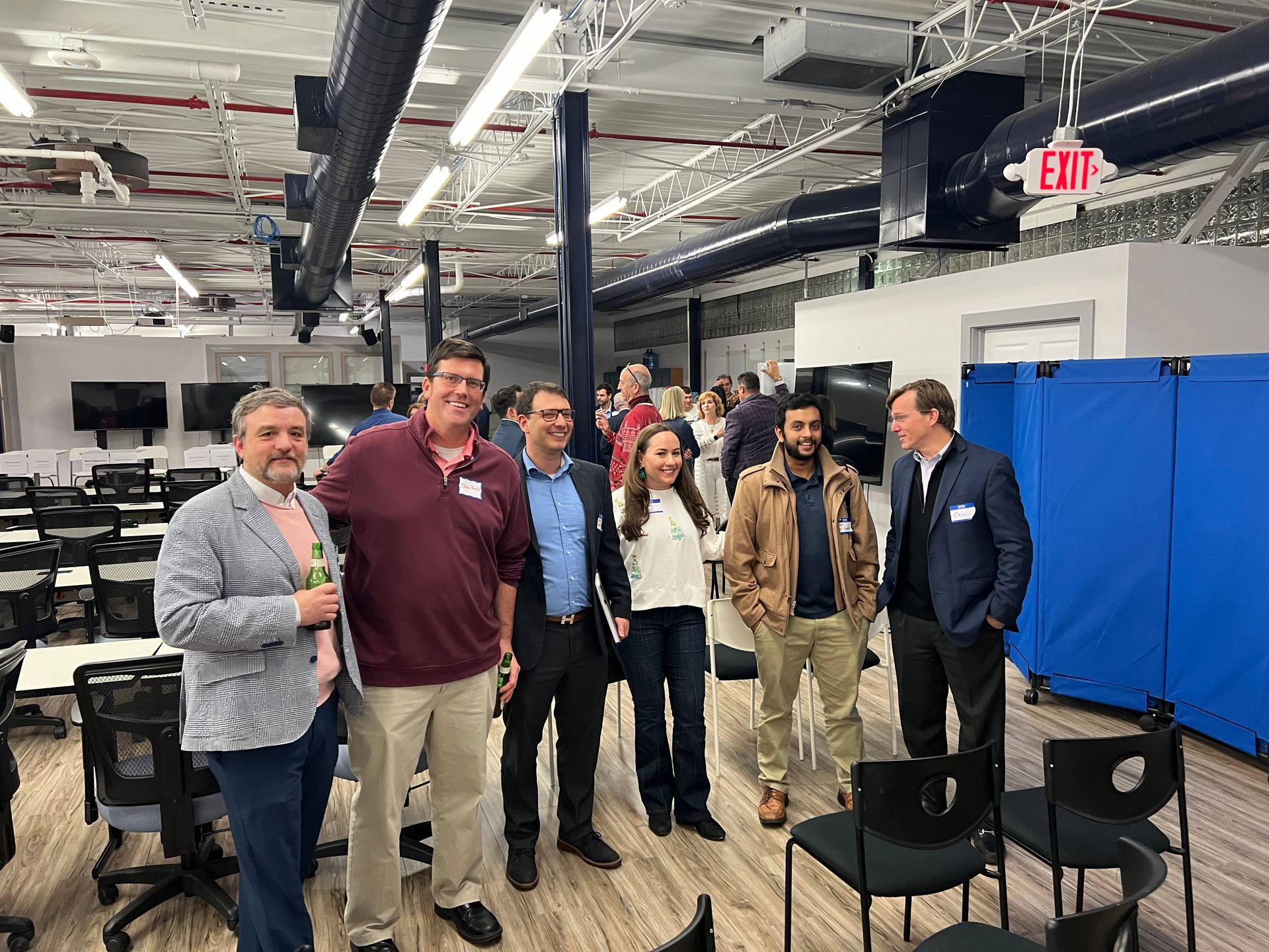 Group of people in a modern office setting. Some are smiling, looking at the camera. Black chairs and desks in the background.