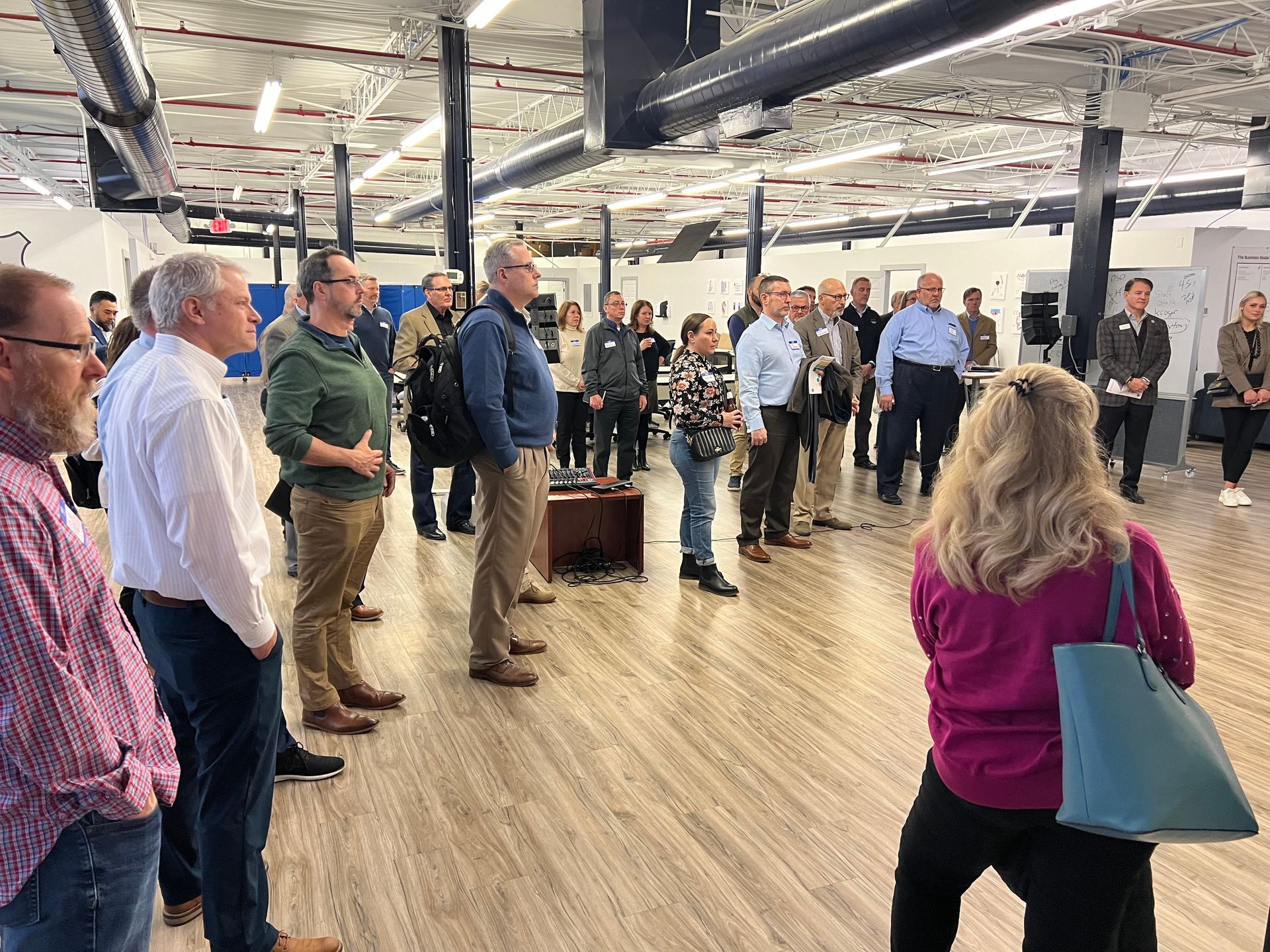 Group of people in an open office space; some are listening to someone, others standing casually.