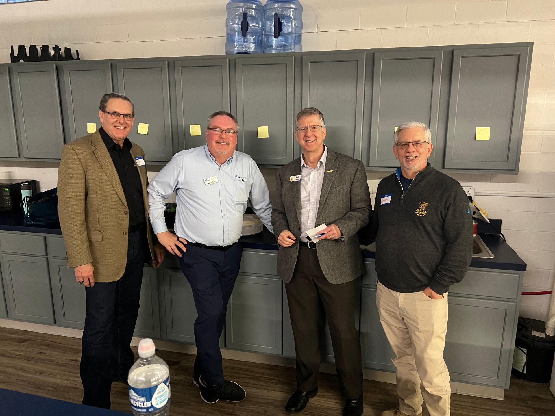 Four men standing by cabinets. They are smiling and appear to be at an event.