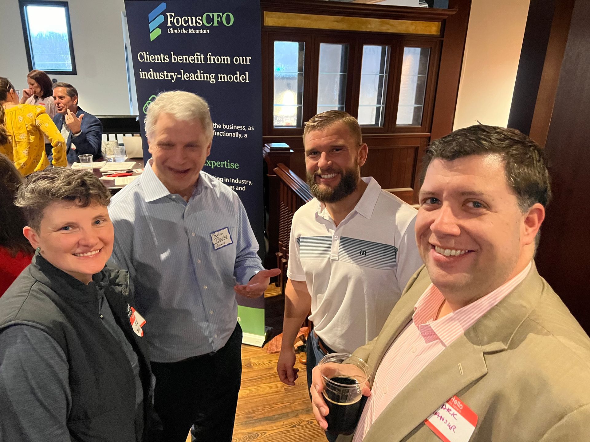 Four people smiling and talking at an event; two men and two women, indoors with a banner.