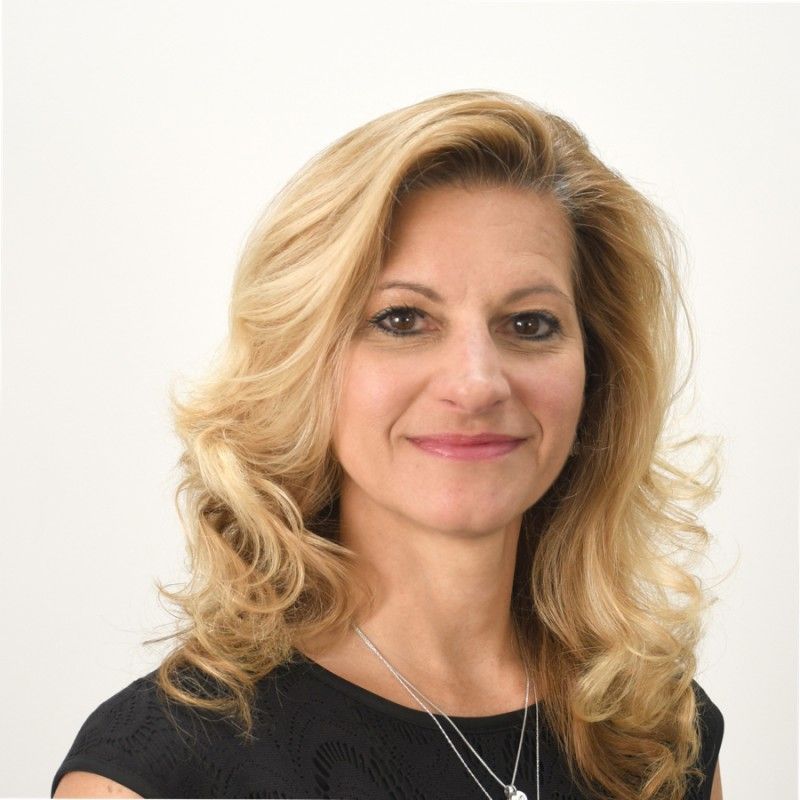 Jennifer Panepinto. Woman with blonde wavy hair smiling, wearing a black top, necklace; against a white background.