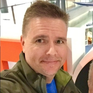 Daron Fender. Man with short brown hair, wearing a green jacket and blue shirt, smiling slightly.