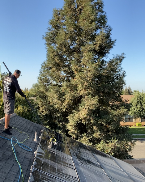 A man is standing on top of a roof cleaning a tree.