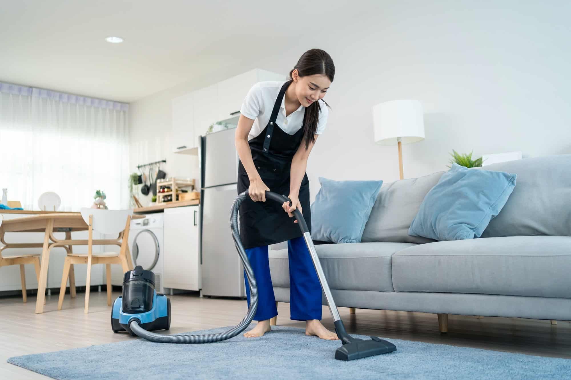 A woman is cleaning the floor with a vacuum cleaner in a living room.