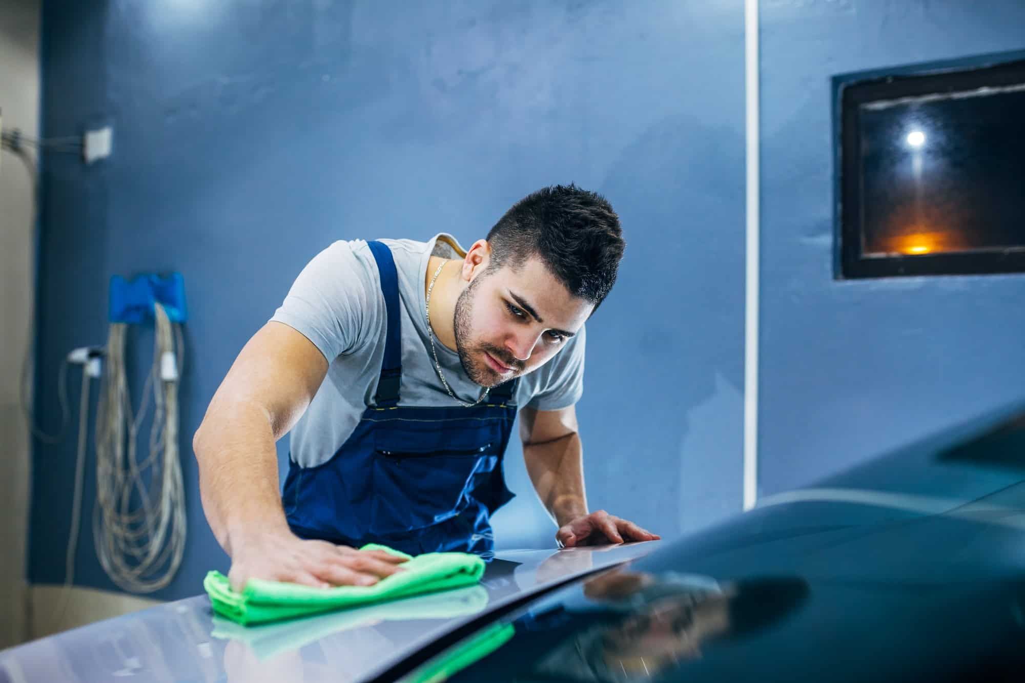 A man is cleaning a car with a cloth in a garage.