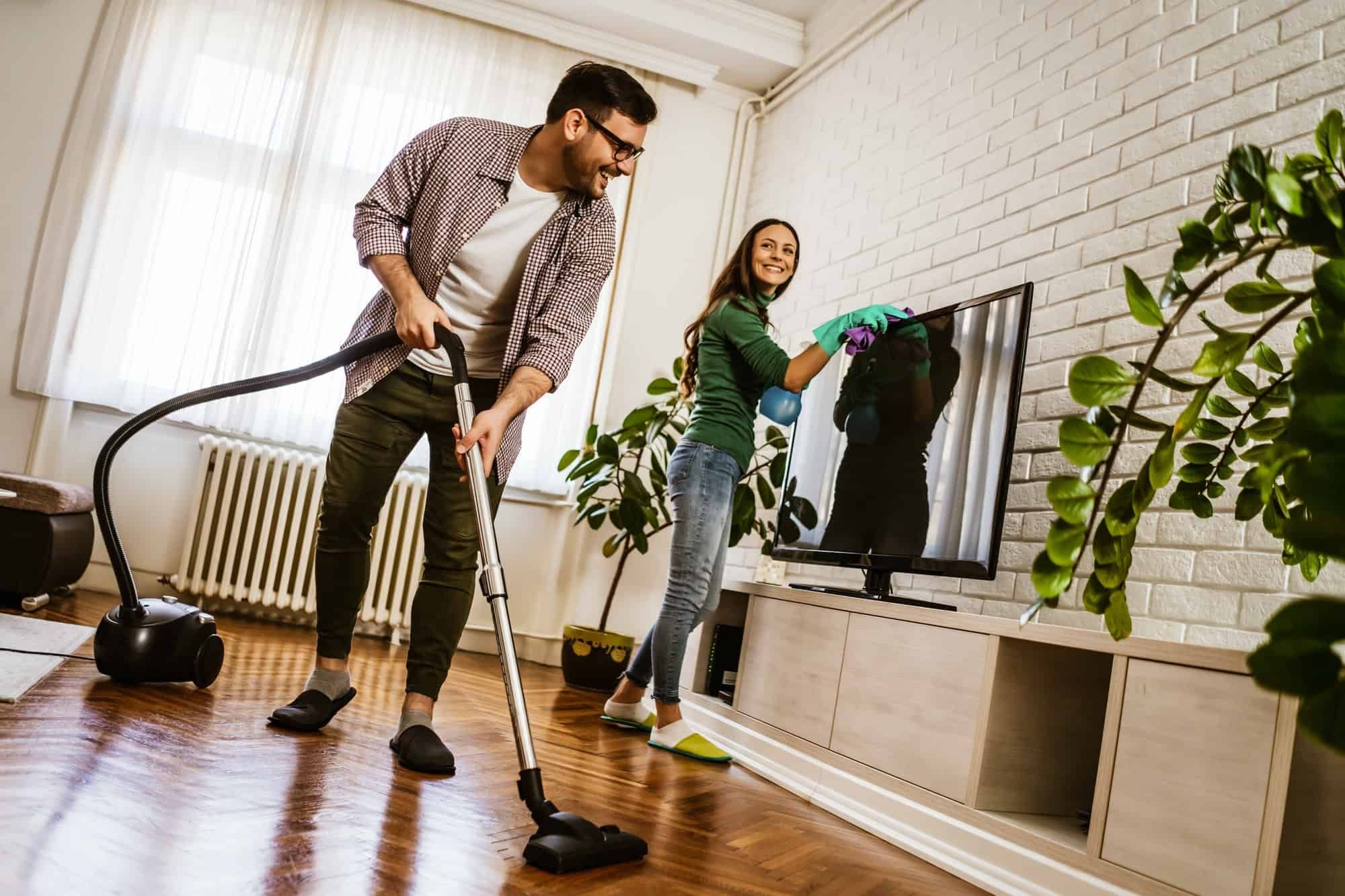 A man and a woman are cleaning a living room with a vacuum cleaner.