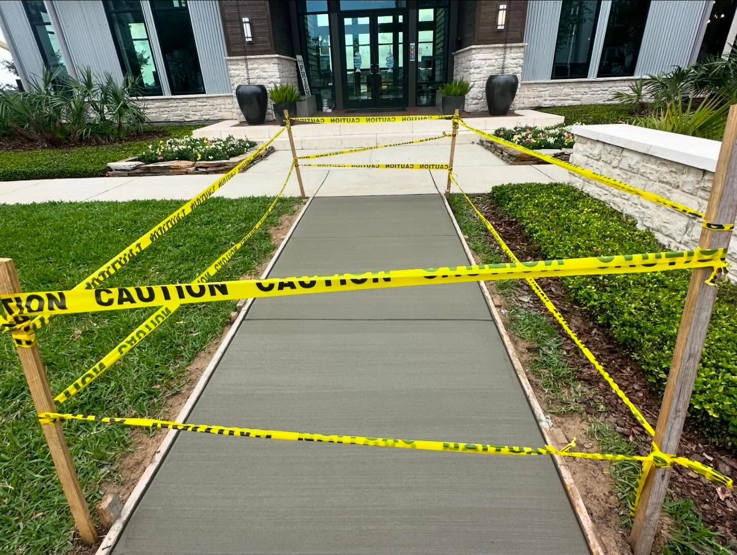 Freshly poured concrete sidewalk blocked by caution tape. Building entrance in background.
