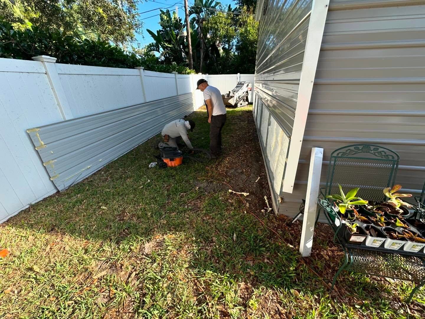 Two people installing metal panels beside a white fence and building on a grassy area.