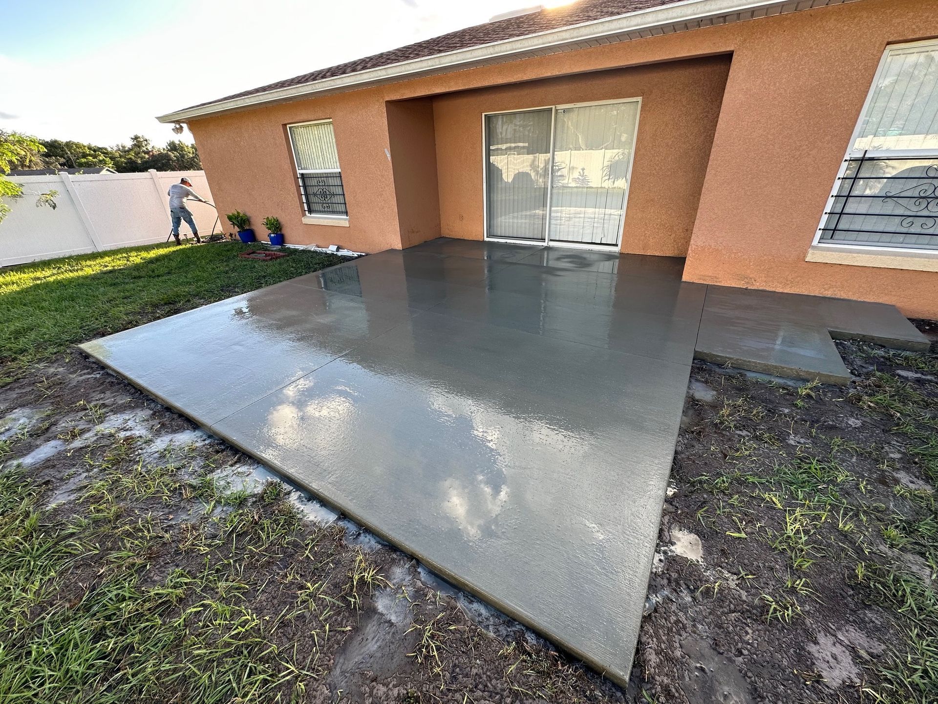 Newly poured concrete patio outside a house. Person spraying water on the concrete.