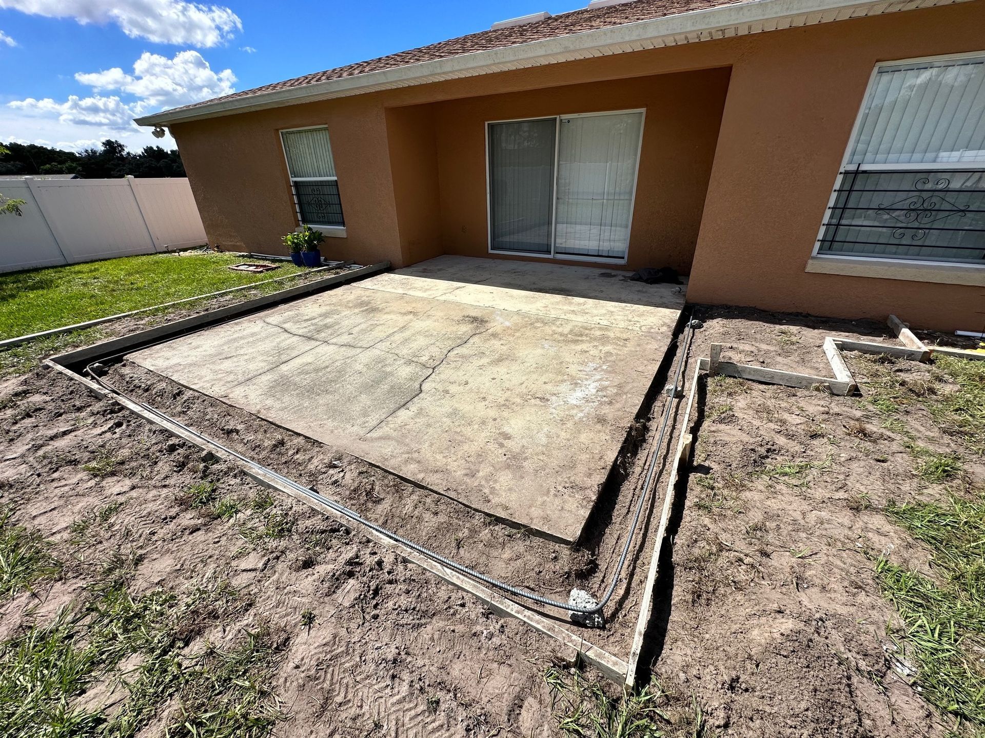 A concrete patio with a surrounding border, next to a tan house with a sliding glass door and windows.