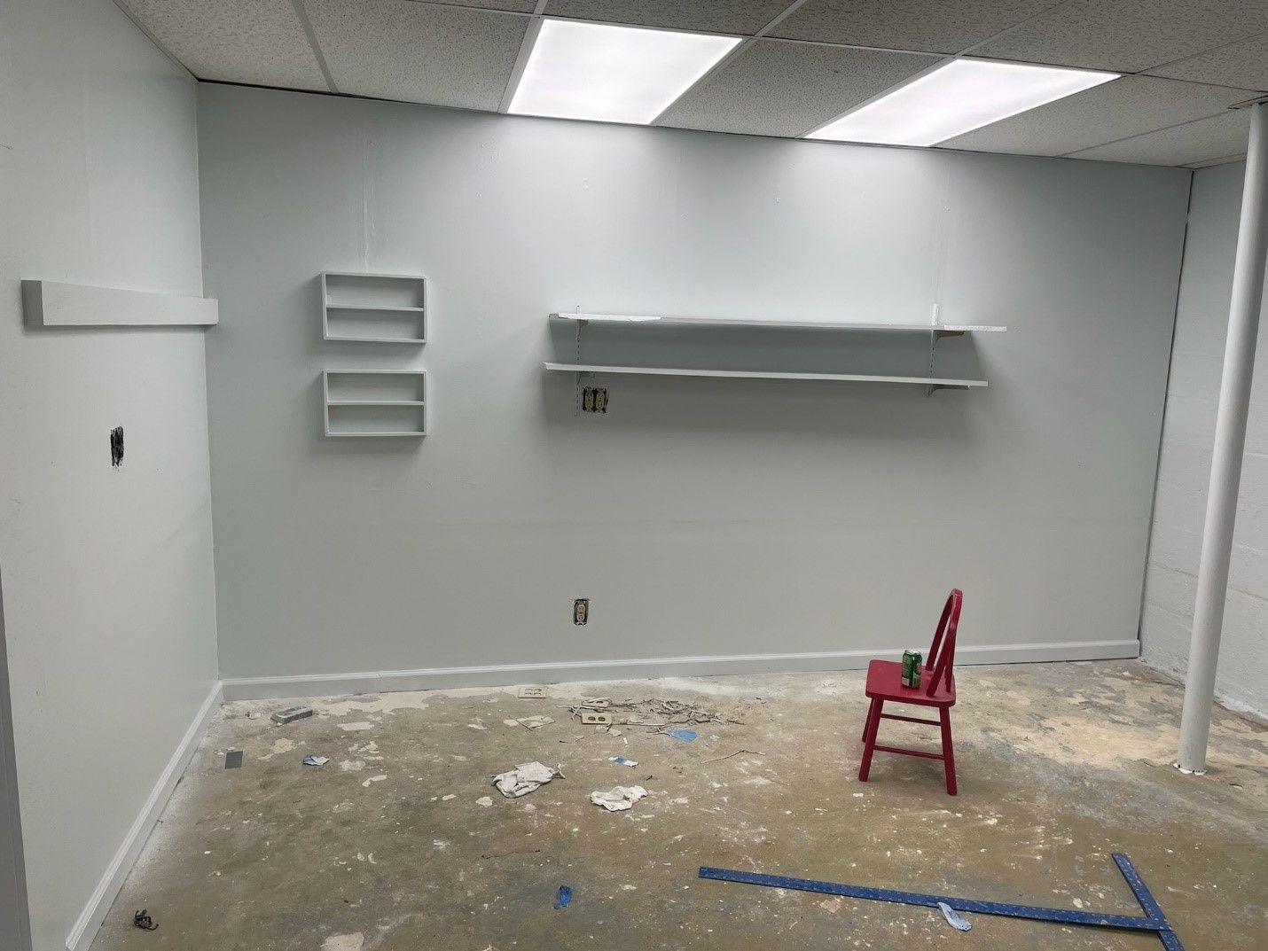 An empty room with a red chair and shelves on the wall.
