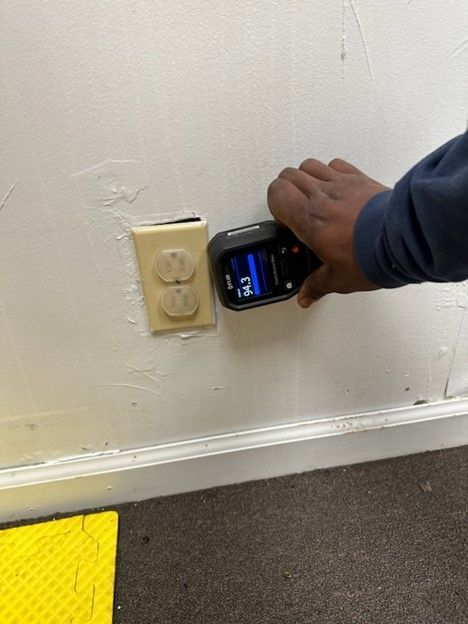 A person is holding a device in front of an electrical outlet on a wall.