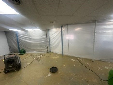 A room with a white tarp on the wall and a fan on the floor.