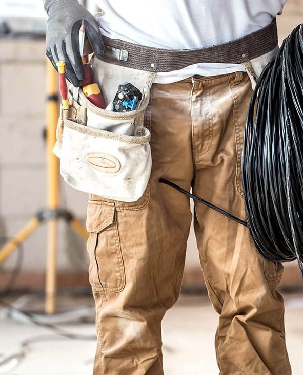 A man wearing a tool belt is holding a roll of wire.