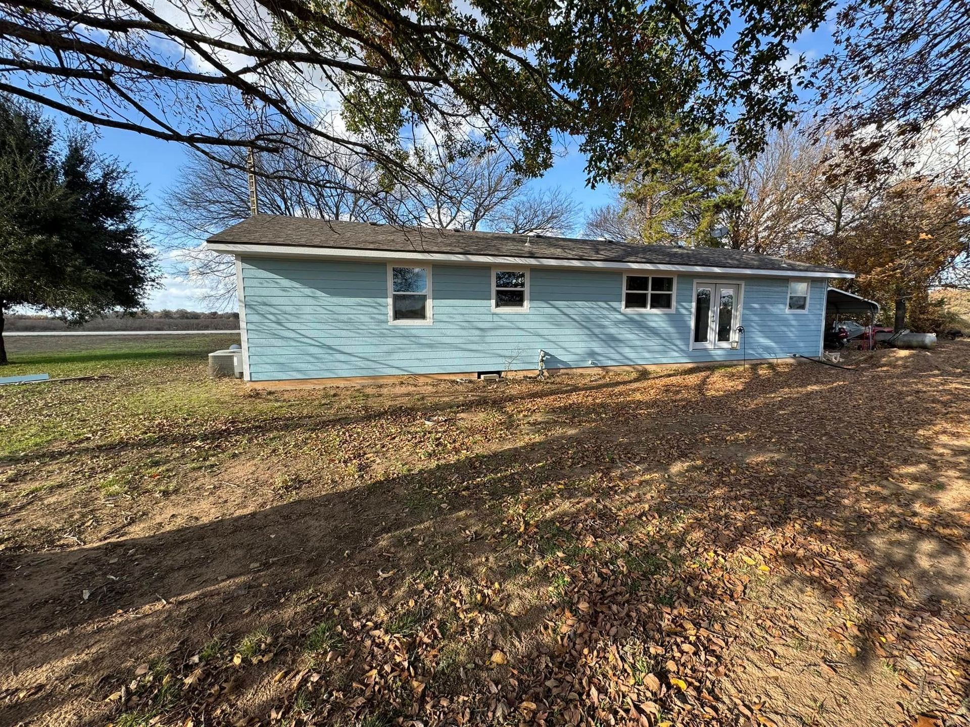 A blue house is sitting on top of a dirt field next to a tree.