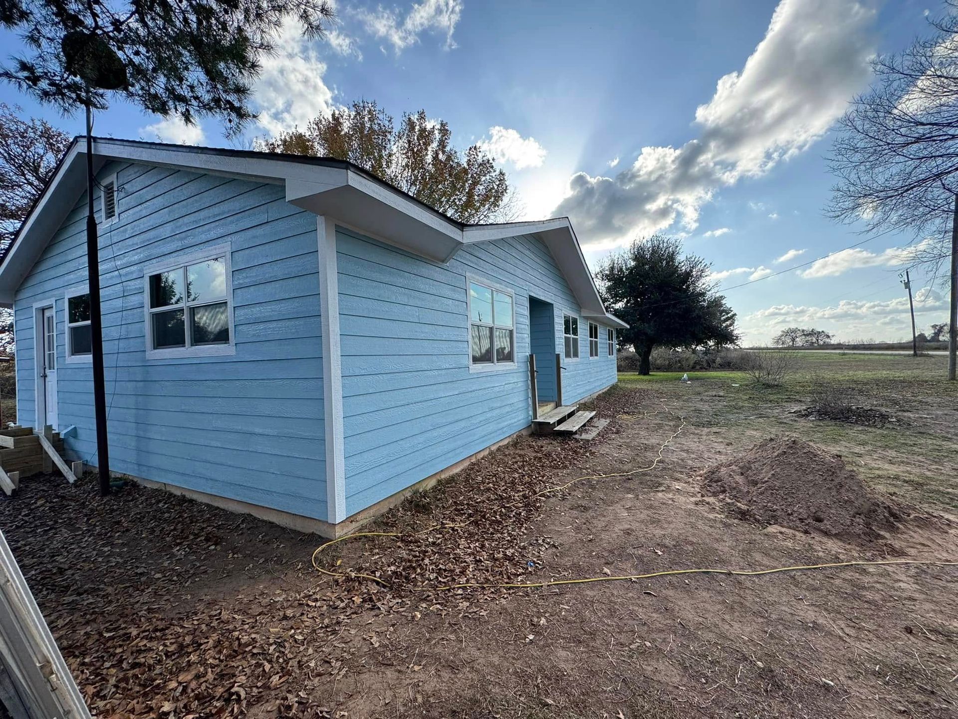 A small blue house is sitting in the middle of a dirt field.