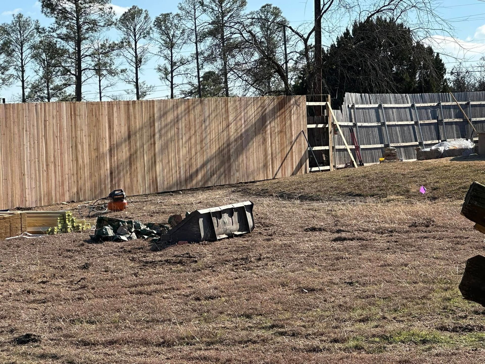 A wooden fence is being built in a field with trees in the background.