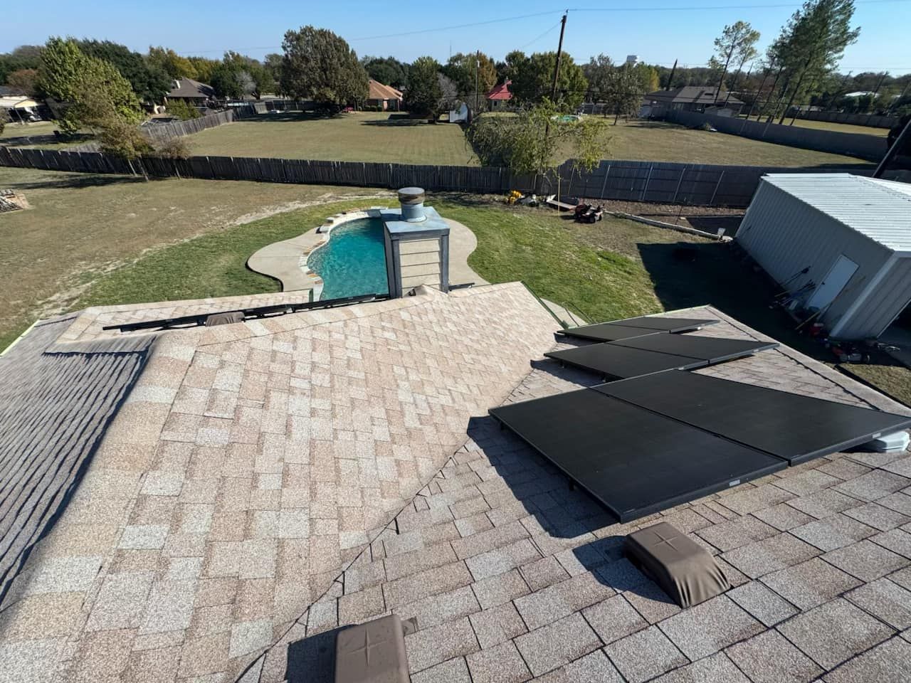 A roof with solar panels on it and a pool in the background
