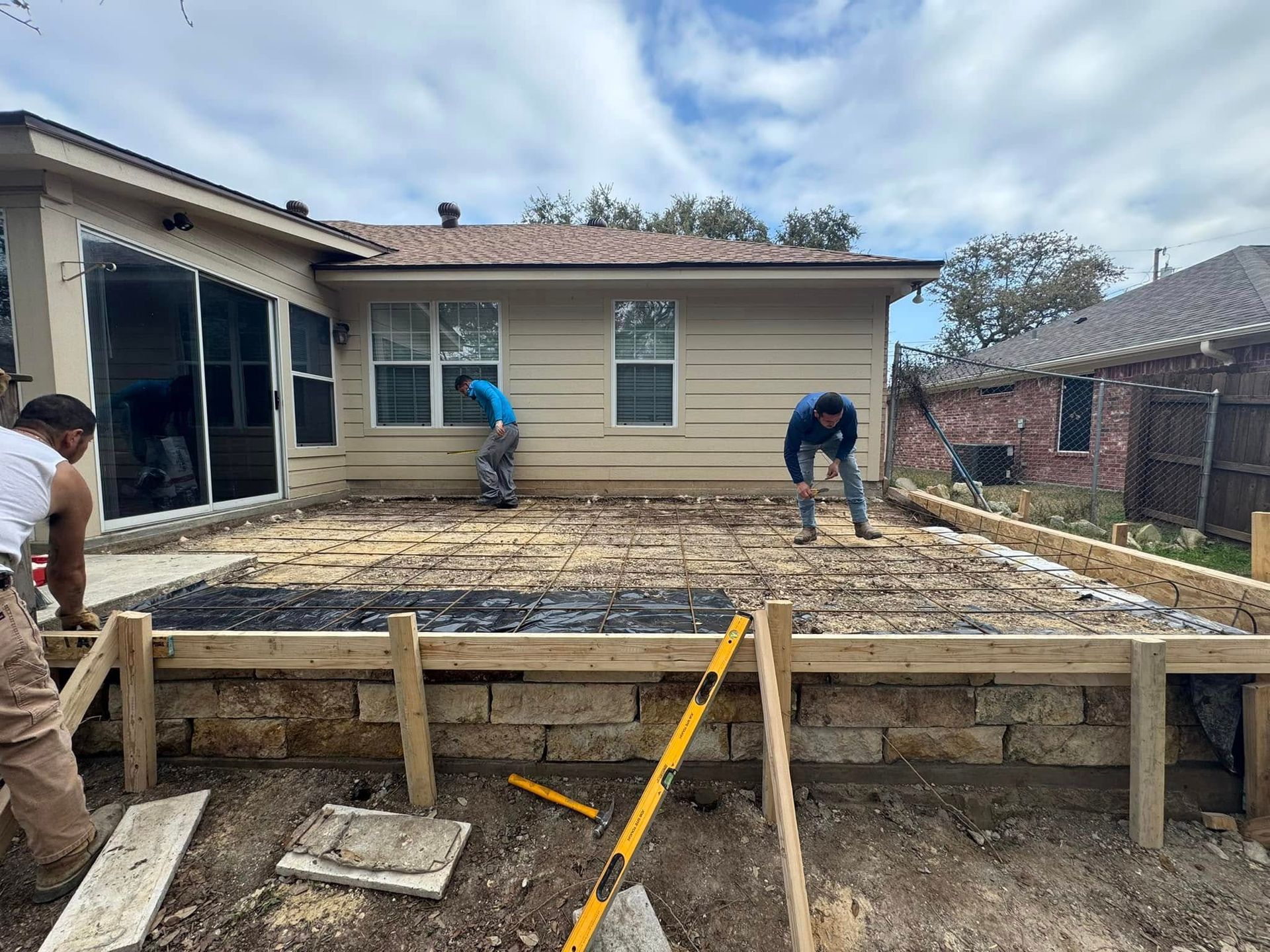 A couple of men are working on a concrete patio in front of a house.