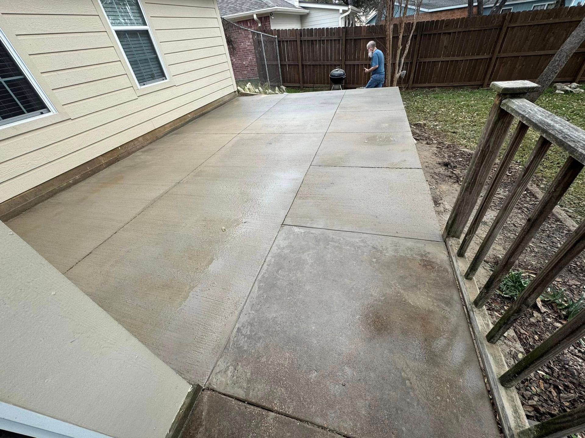 A man is standing on a concrete patio next to a wooden fence.