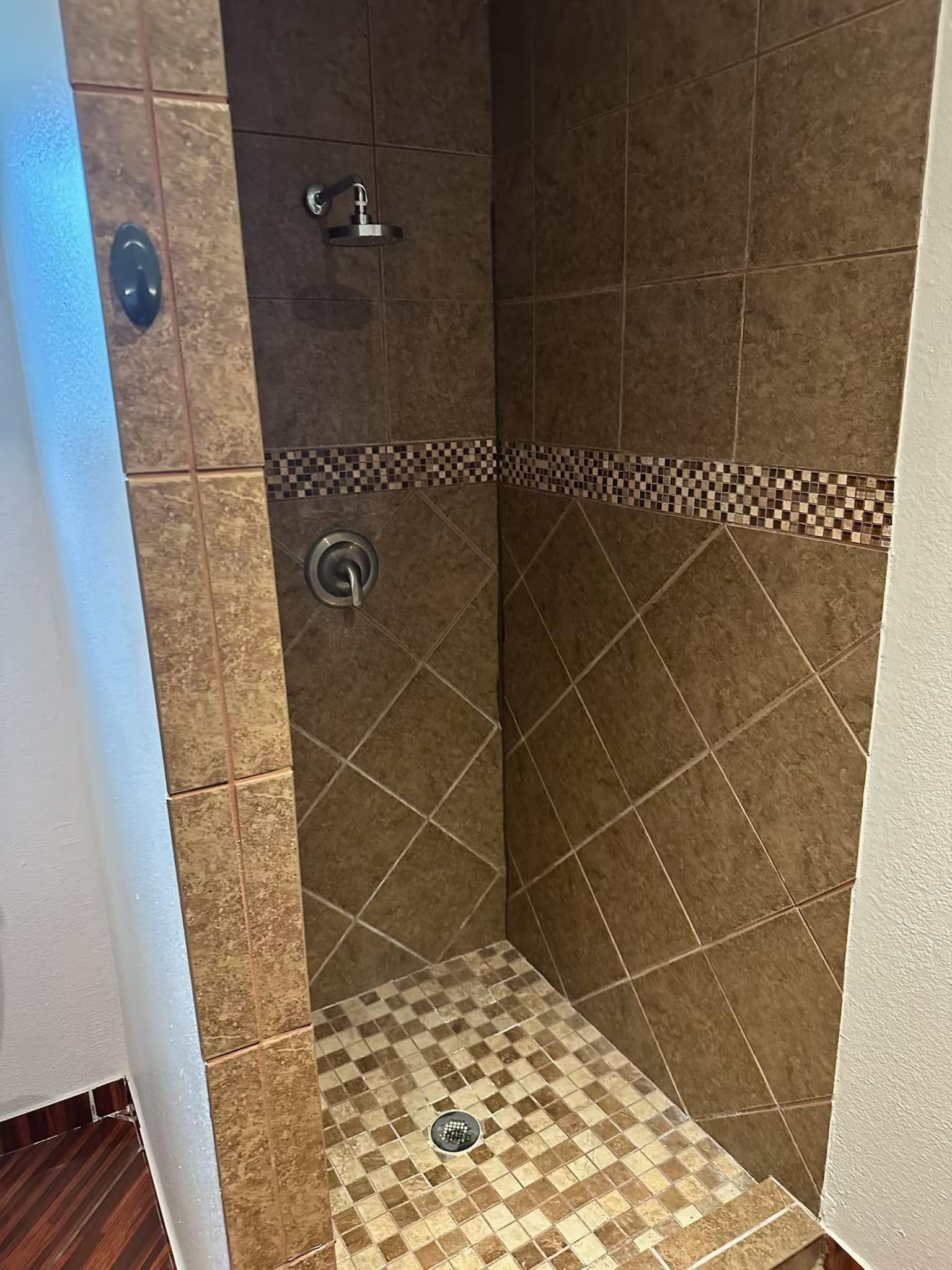 A walk in shower with brown tiles and a faucet in a bathroom.