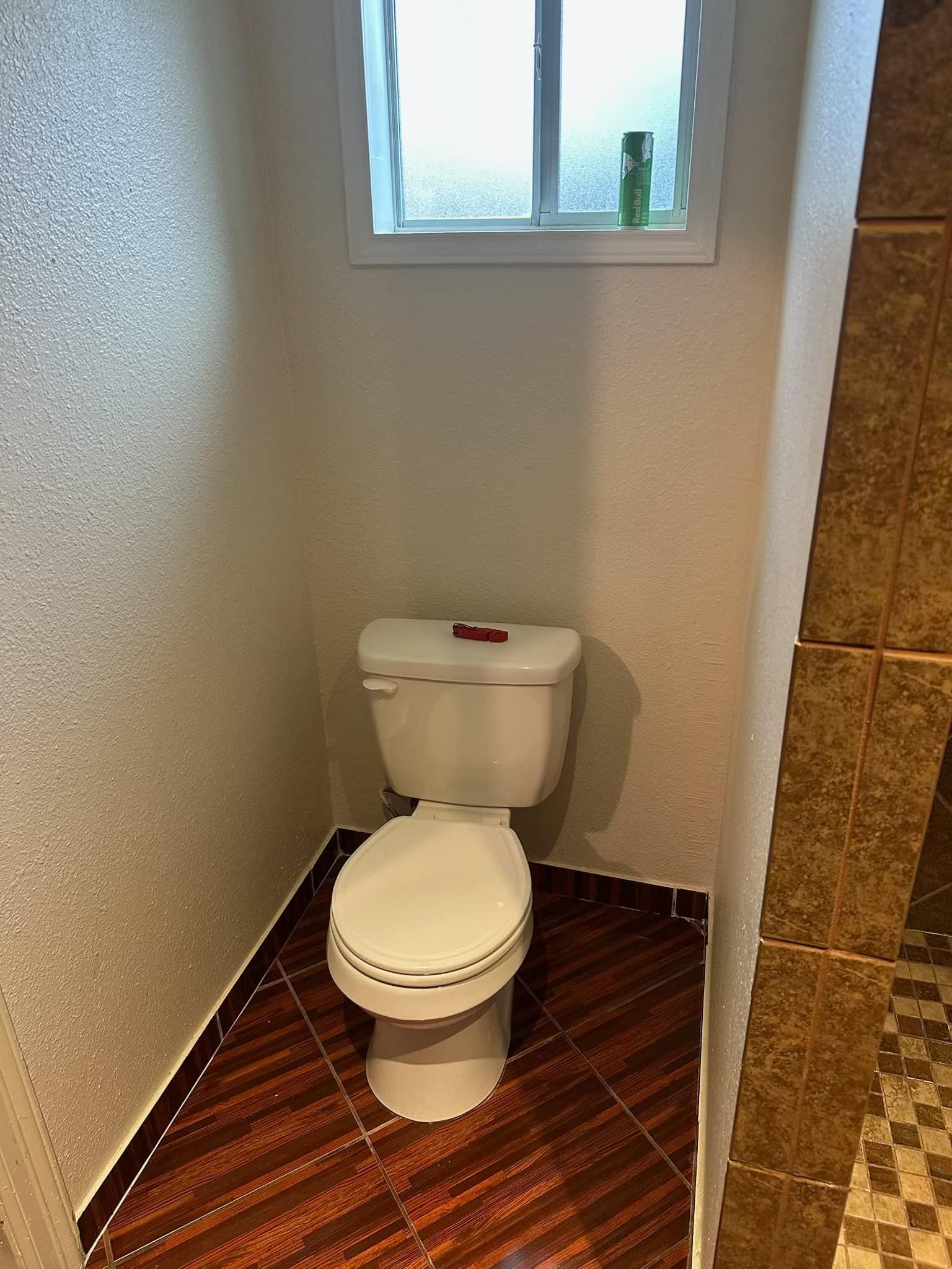 A toilet is sitting in a bathroom next to a window.