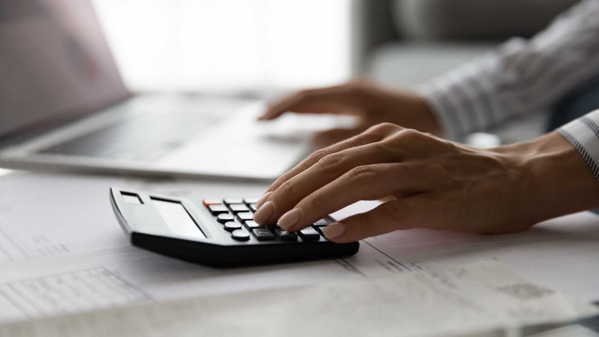 Hands using a calculator and laptop for calculations, possibly financial or accounting tasks.