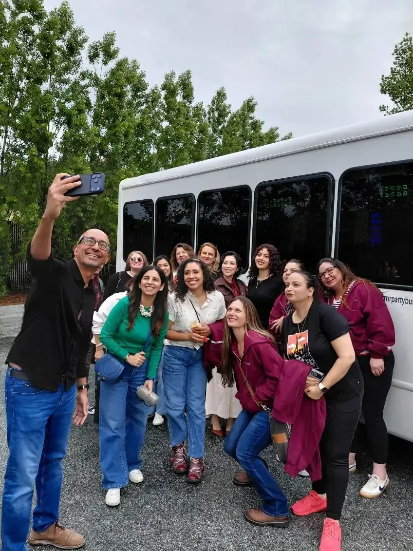 Group posing for a selfie beside a white van, smiling outdoors on a gravel lot.