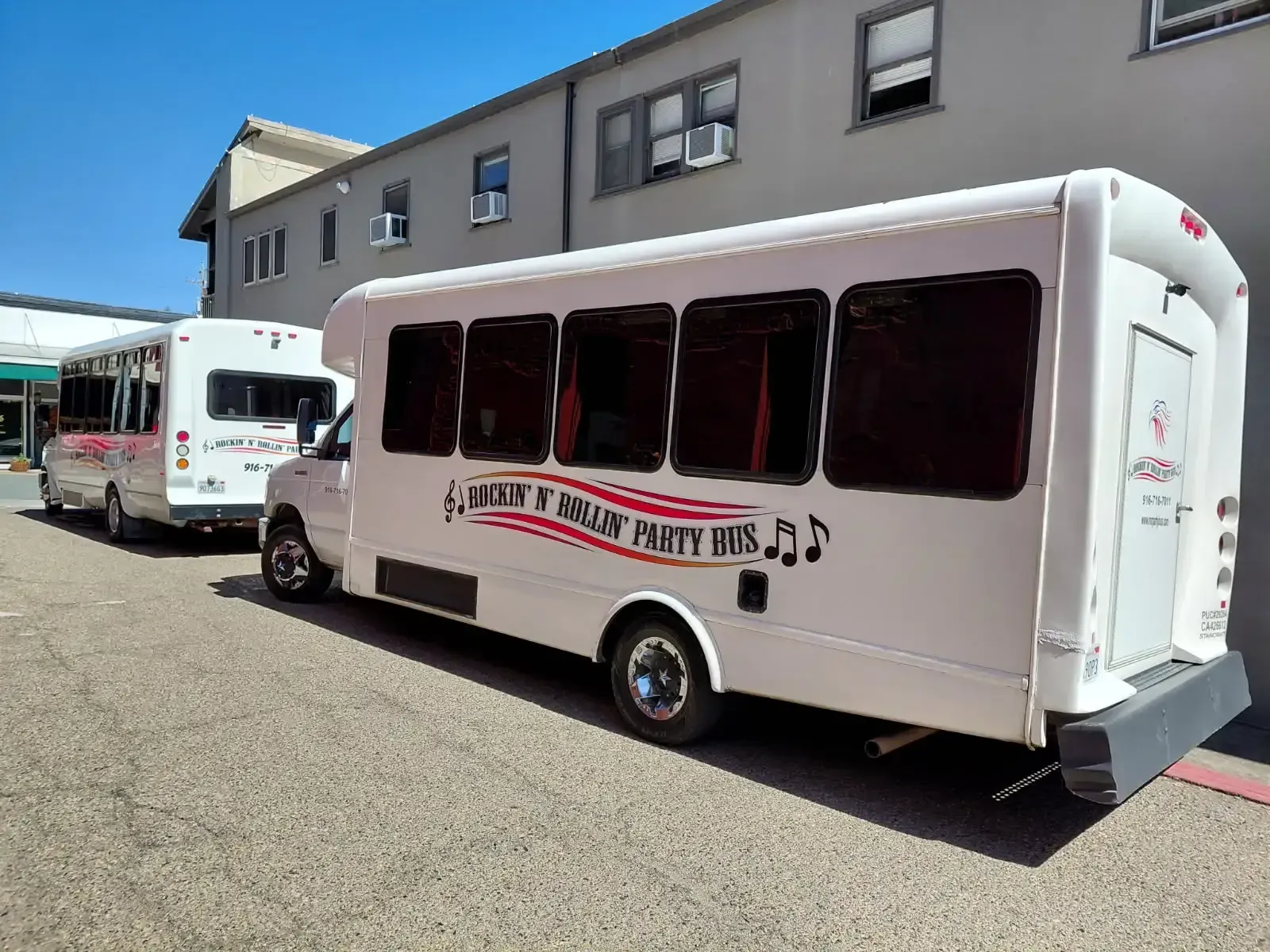 White party bus with red lettering parked outside a gray building in a gravel lot