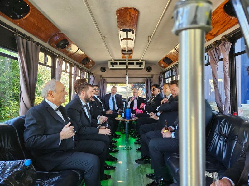 Wedding party in a decorated bus, smiling guests raise glasses around a bride in a white dress