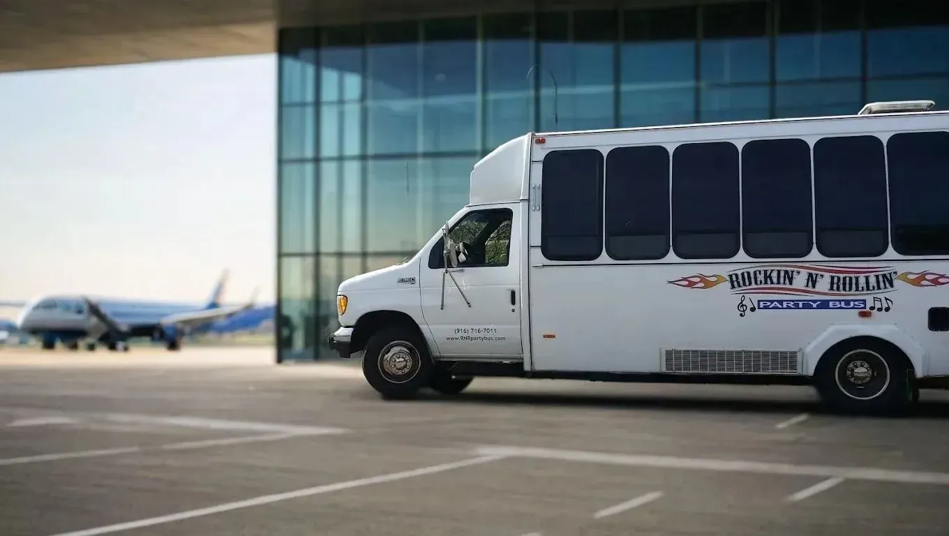 White shuttle van parked beside airport terminal with planes visible in the background