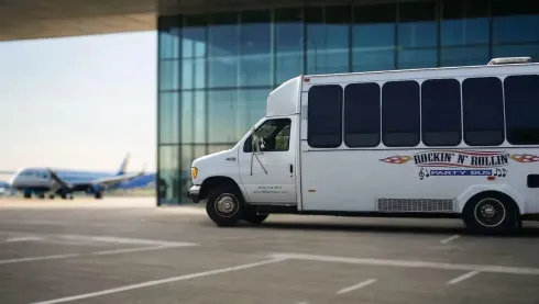 White shuttle bus parked outside an airport terminal with a plane in the background