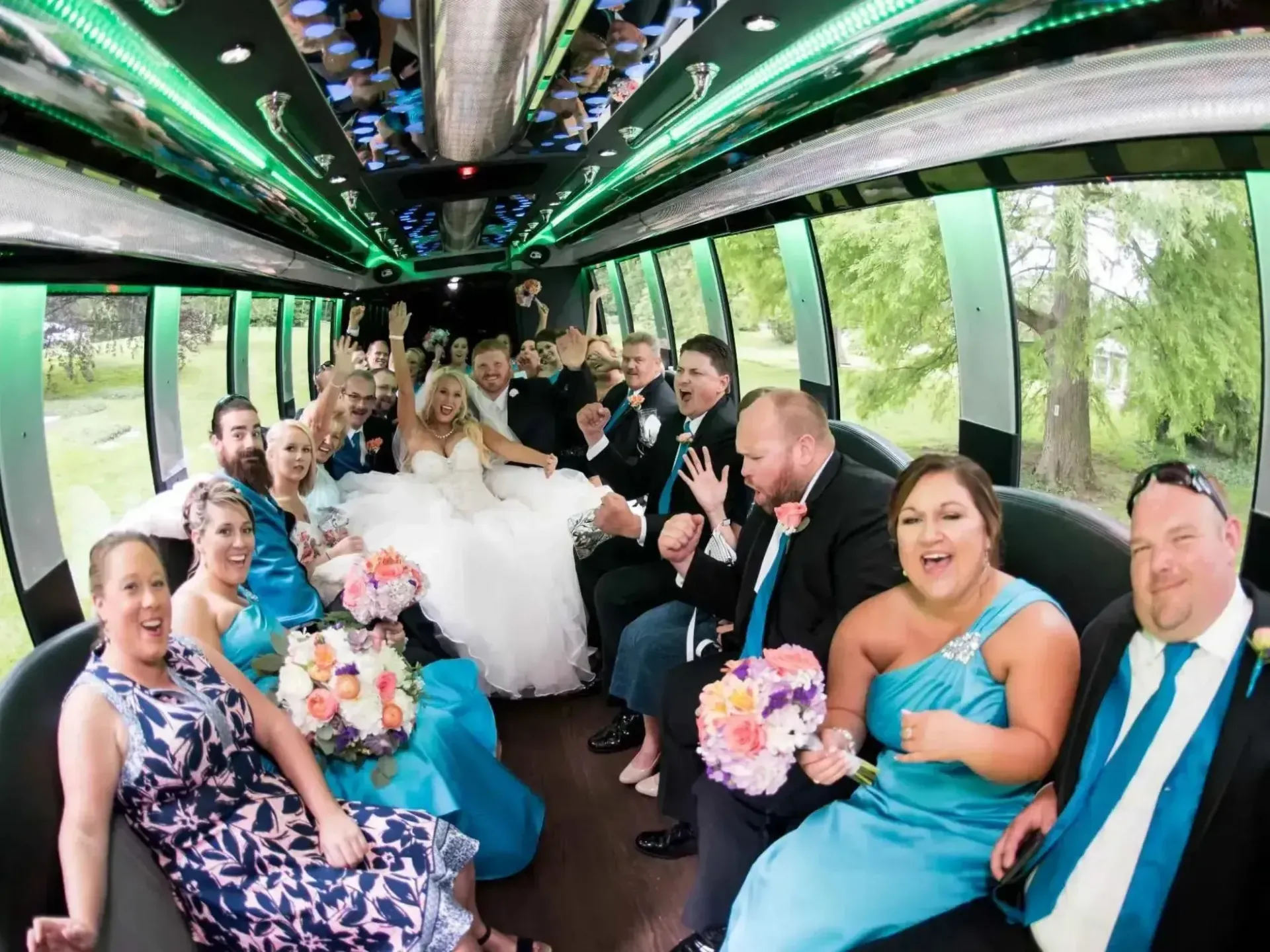 Wedding party in a decorated bus, smiling and toasting with bouquets and a bride in white.