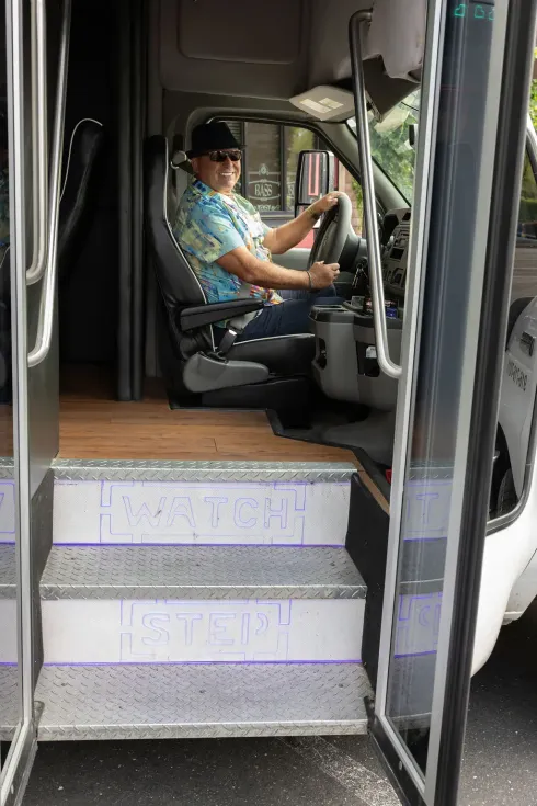 Bus driver seated at the wheel, viewed through the open bus door and steps.