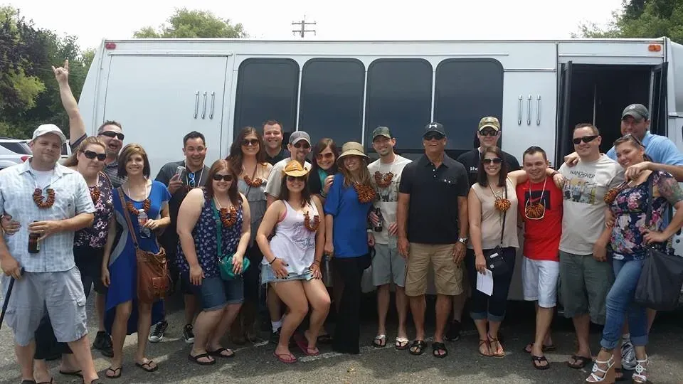 Group of people posing in front of a white bus at an outdoor event