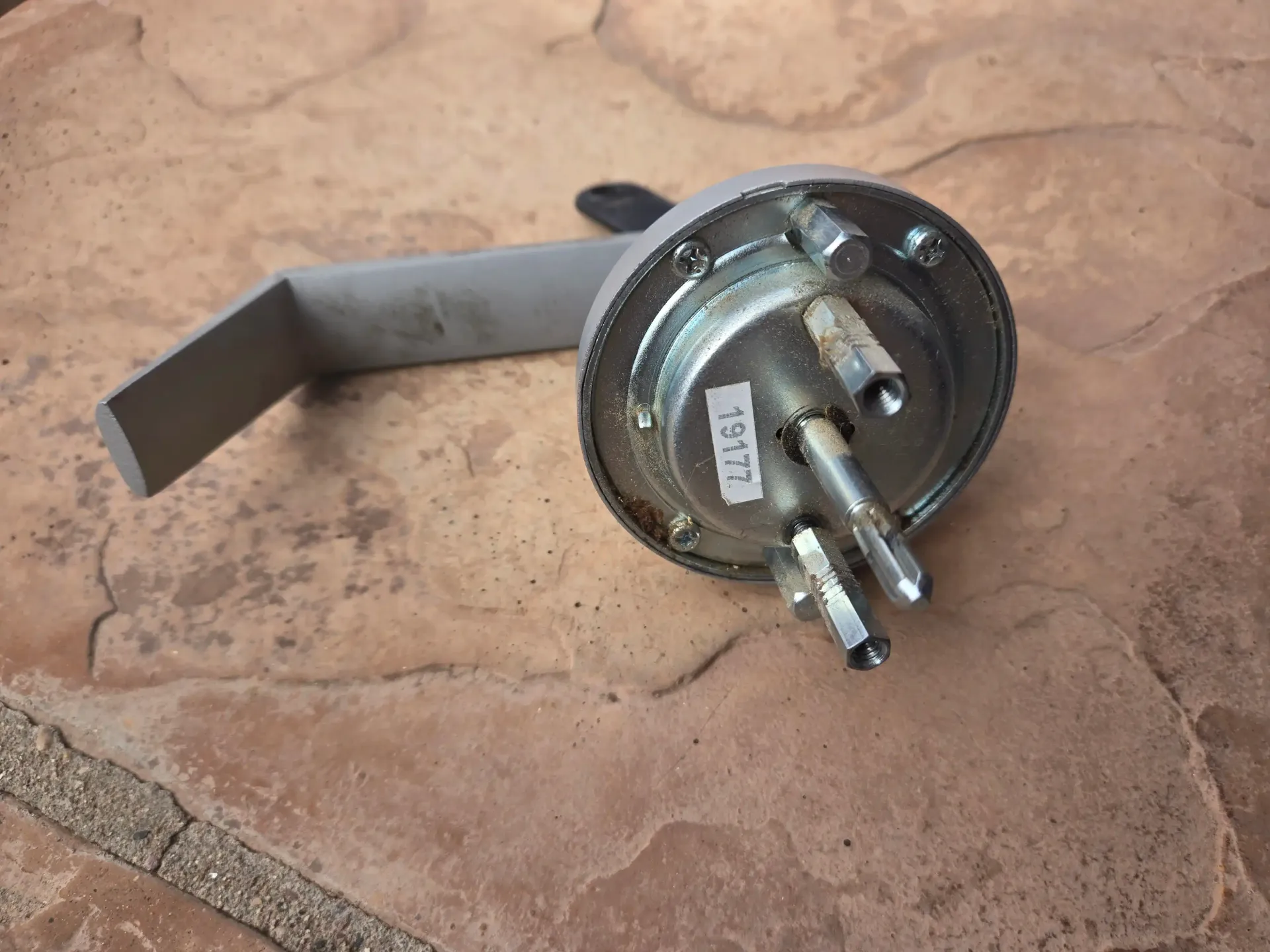 Metal latch lock mechanism on a stone floor, with a circular base and protruding handle.
