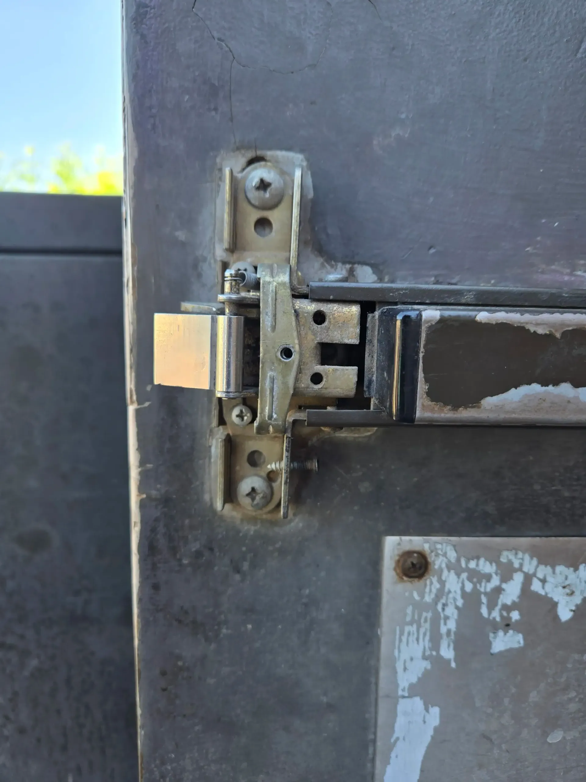 Close-up of a weathered metal gate hinge and latch on a dark painted fence.