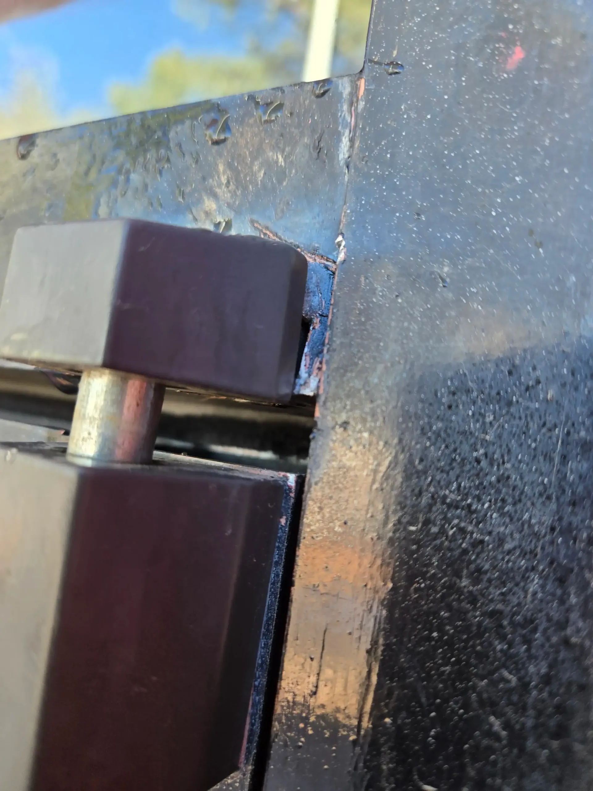 Close-up of a black metal hinge on a weathered painted surface with rust and chipped paint