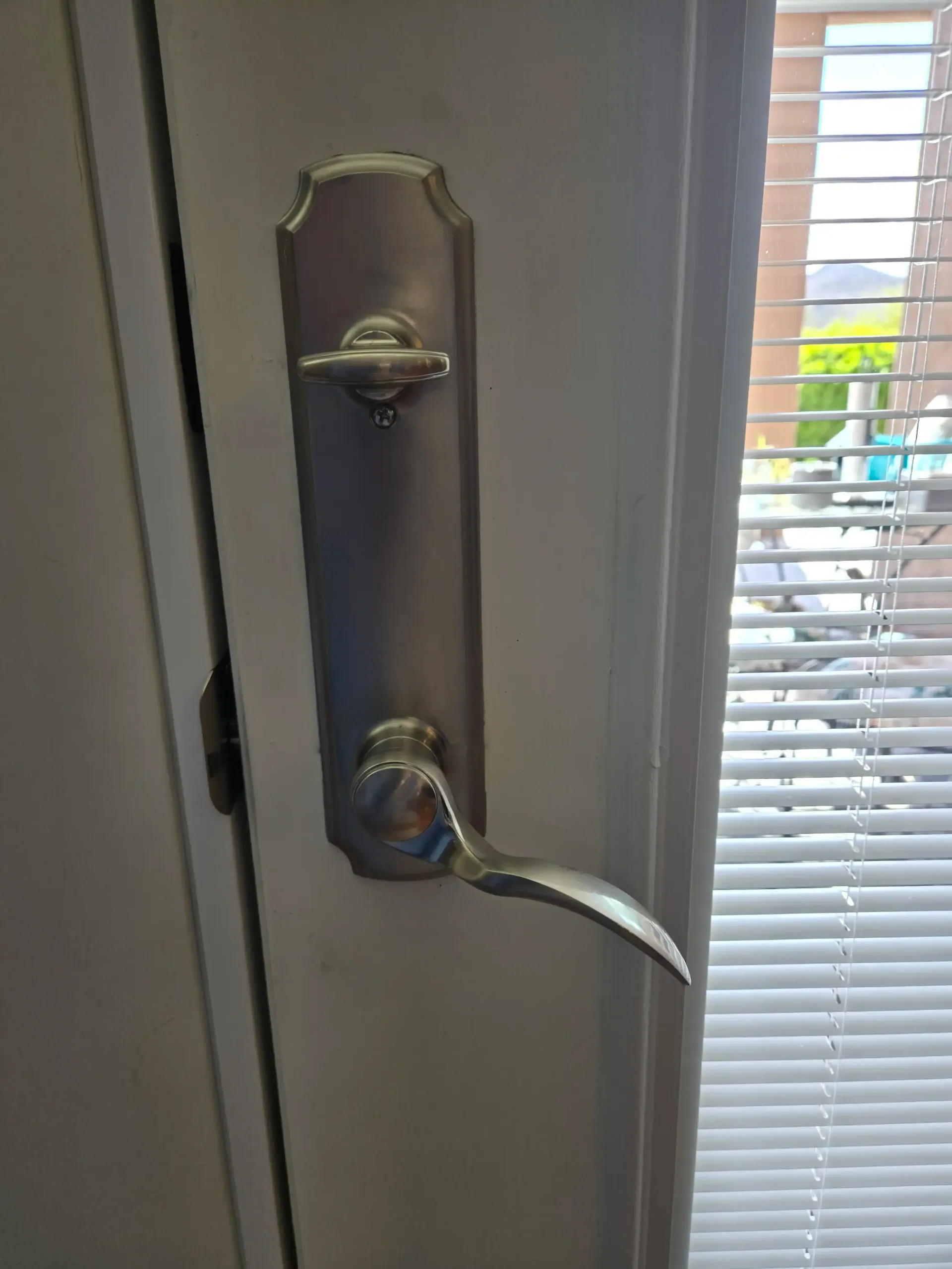 Close-up of a silver door handle and deadbolt on a gray door beside window blinds.