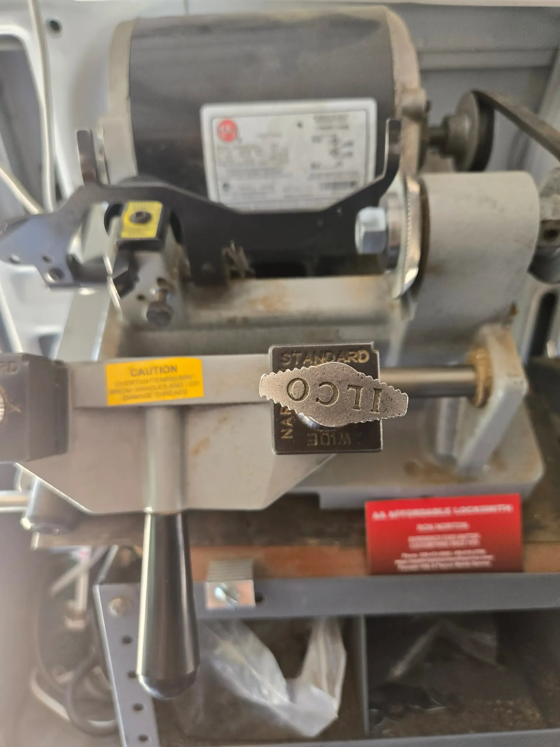 Close-up of a metal bench grinder with attached wire wheel and safety labels.