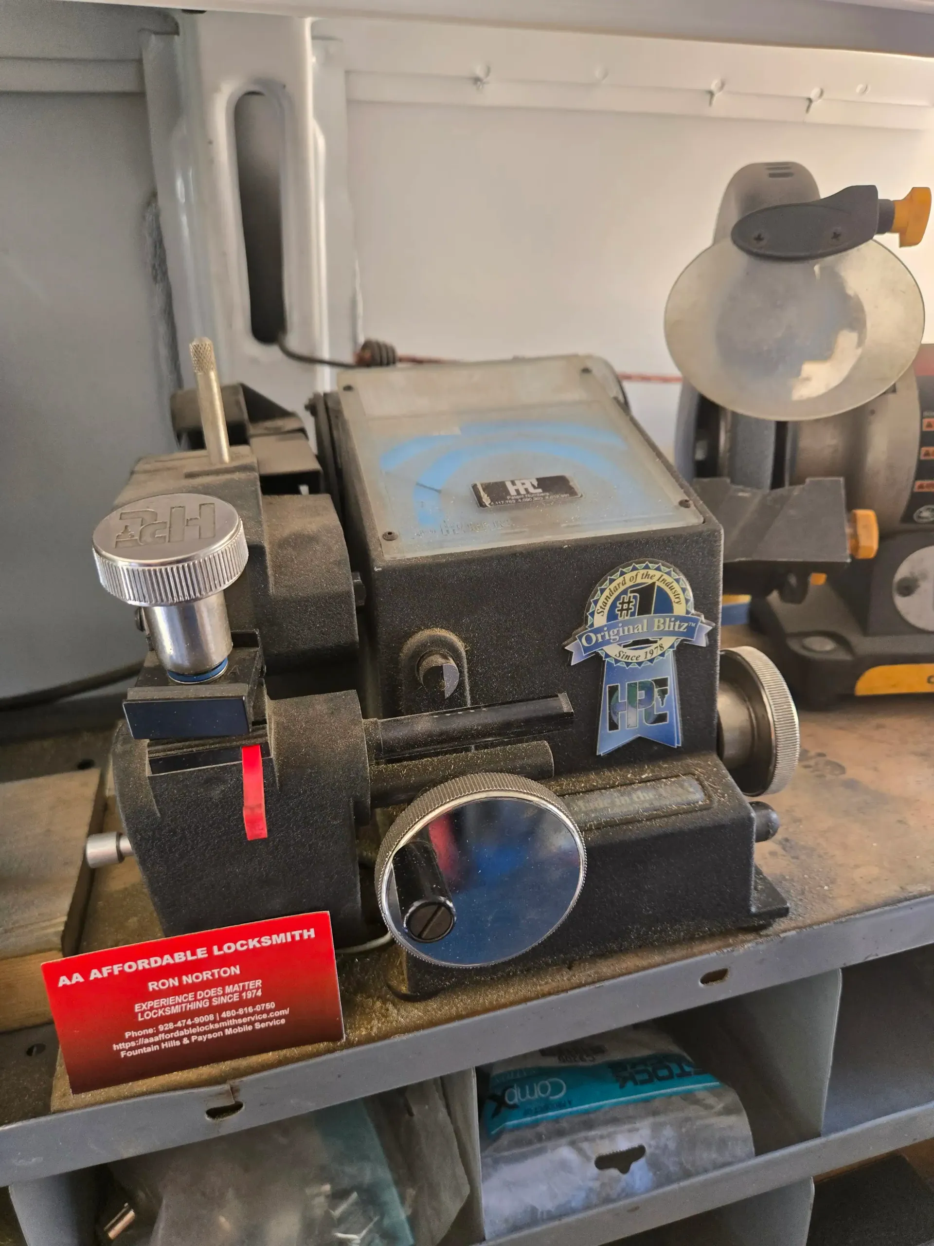 Black tabletop machine with knobs and a clear reservoir, set on a shelf in a workshop-like space