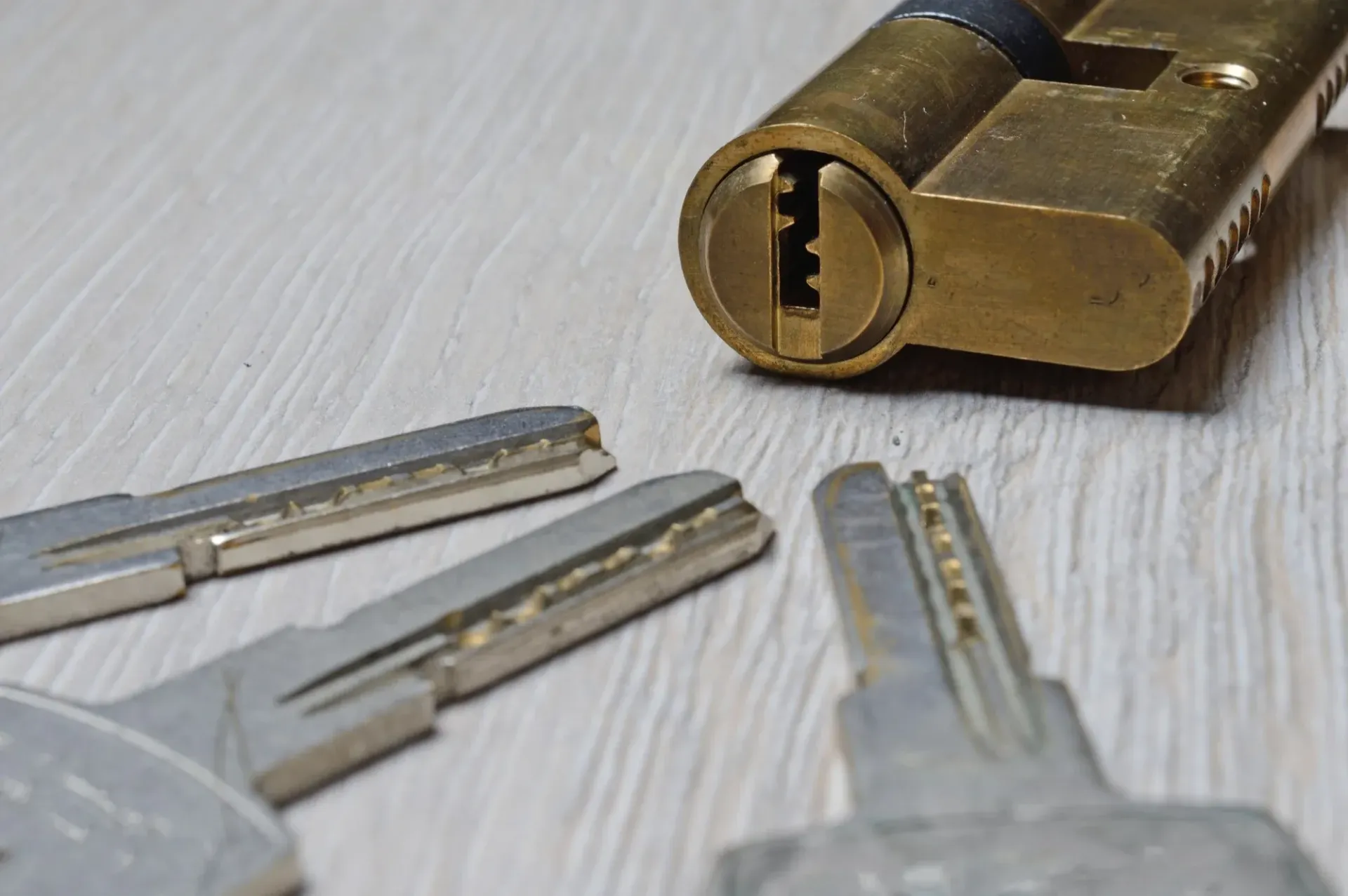 Three metal keys beside a brass lock cylinder on a light gray surface