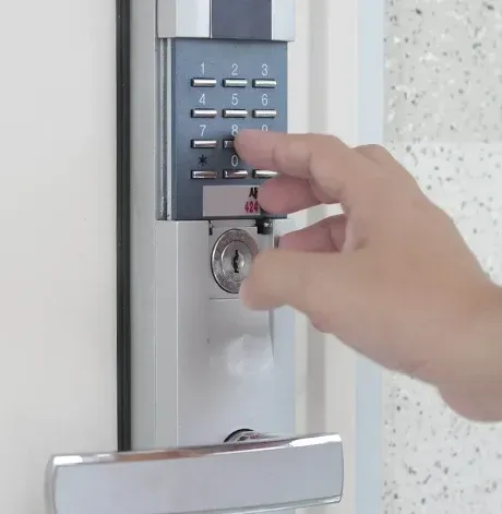 Hand entering a code on a gray door keypad lock with a silver handle below.