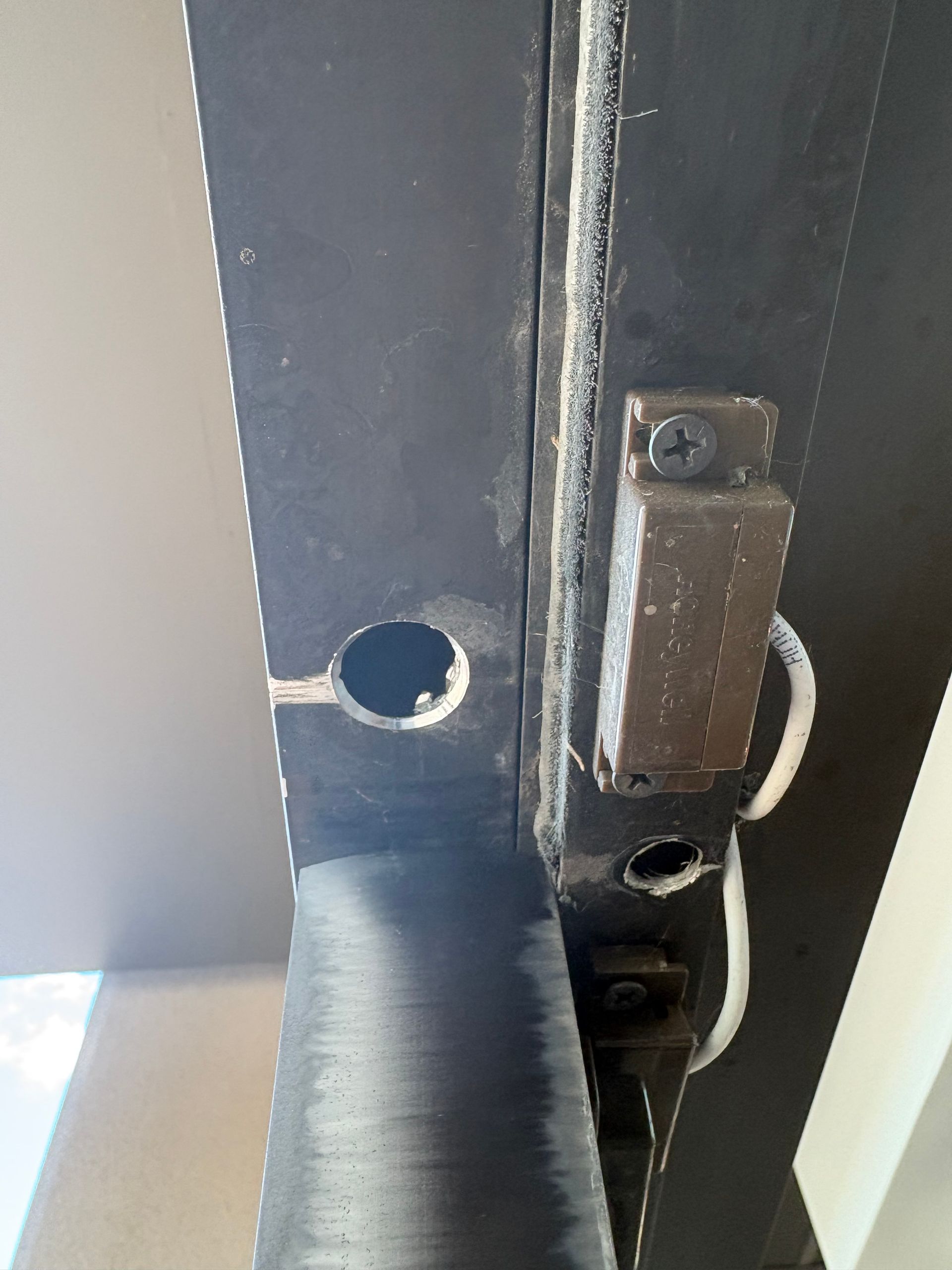 Close-up of a black metal door frame with a latch, holes, and white wiring on the side.
