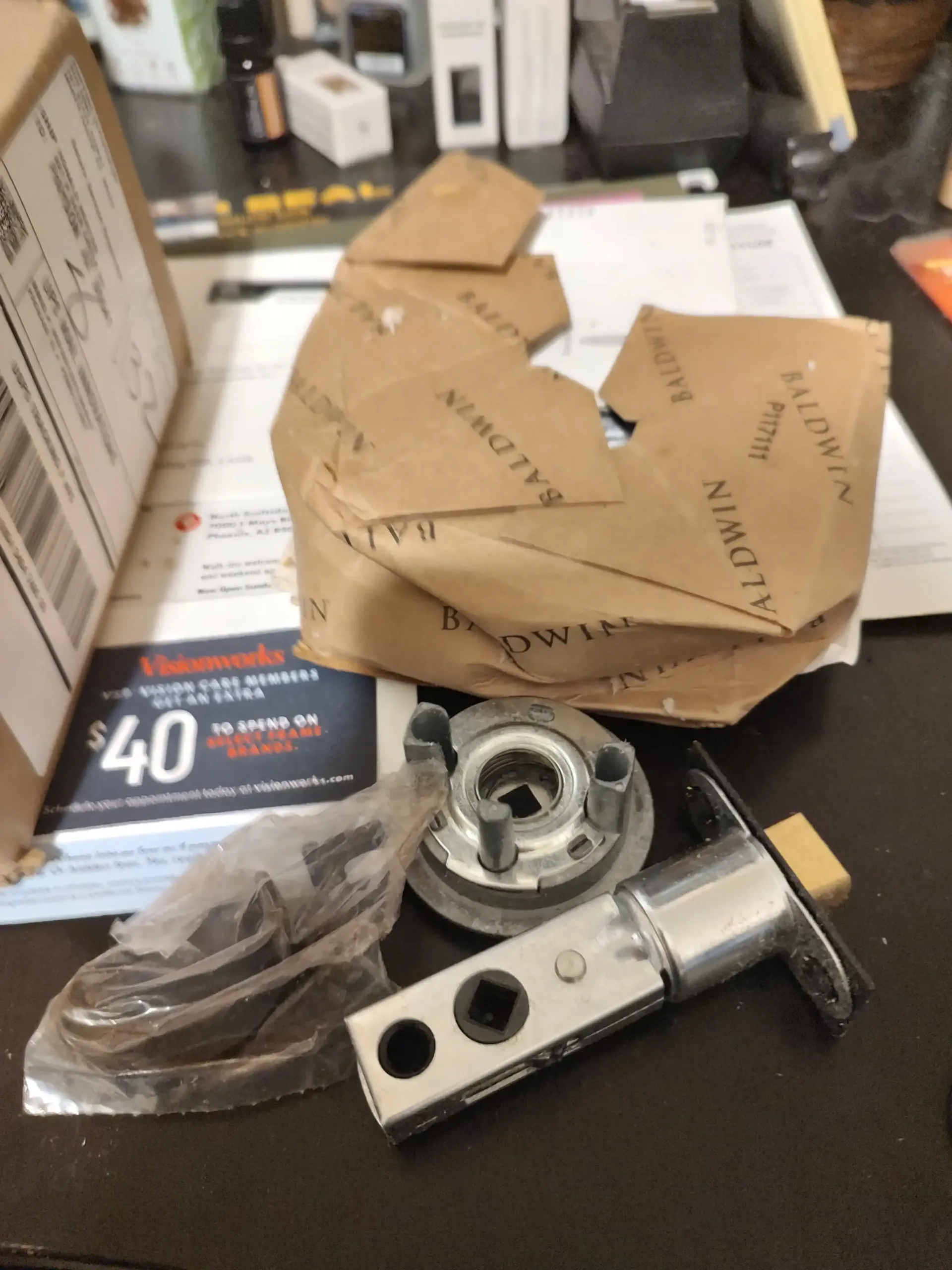 Box of metal hardware parts and packaging on a black tabletop, with a cardboard container in the back