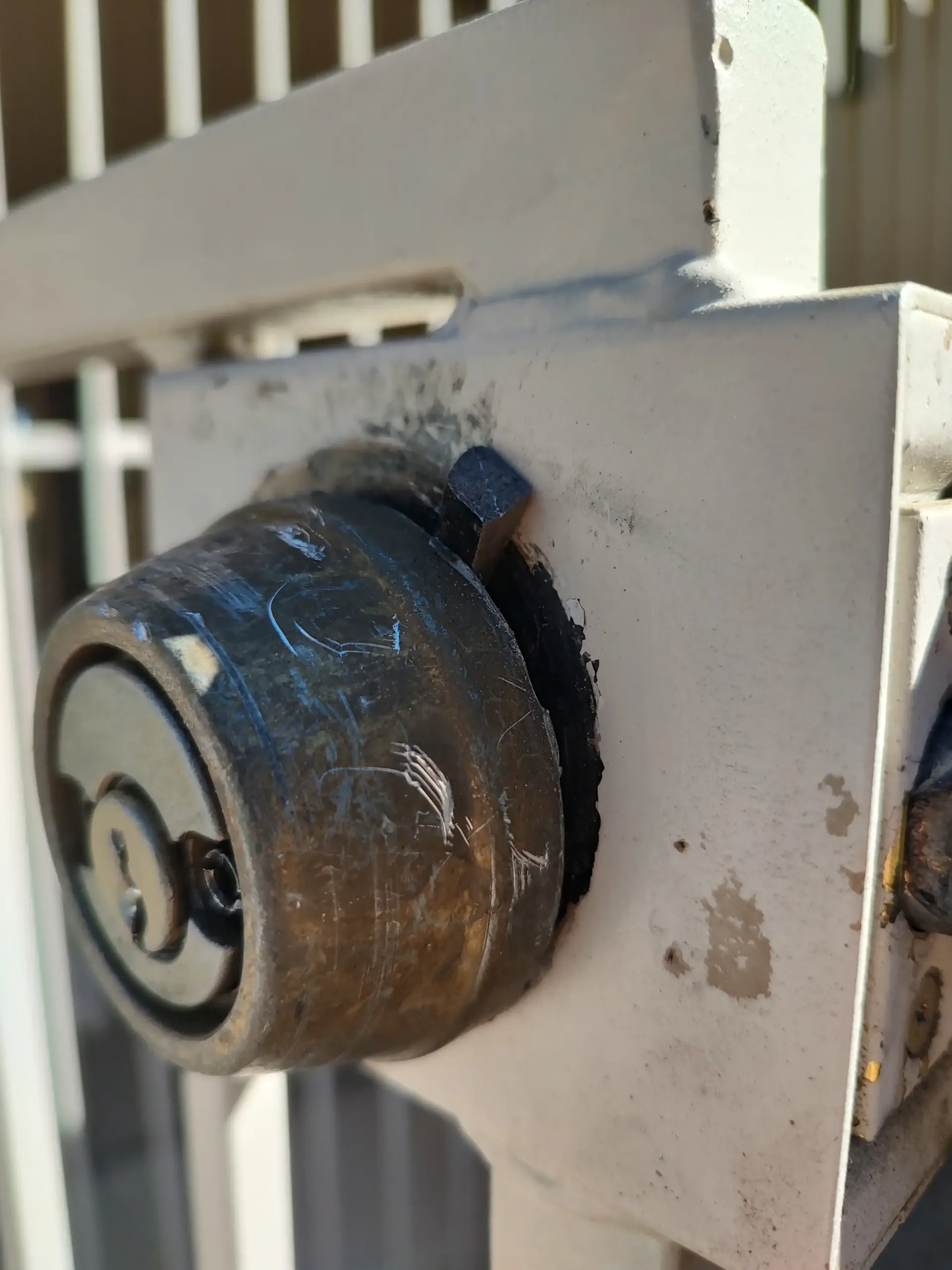 Close-up of a rusted metal door lock on a white painted gate panel