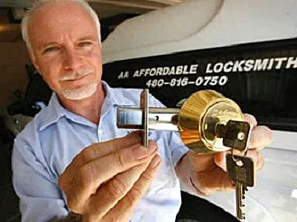 Locksmith holding a brass door lock and key in front of an Affordable Locksmith sign